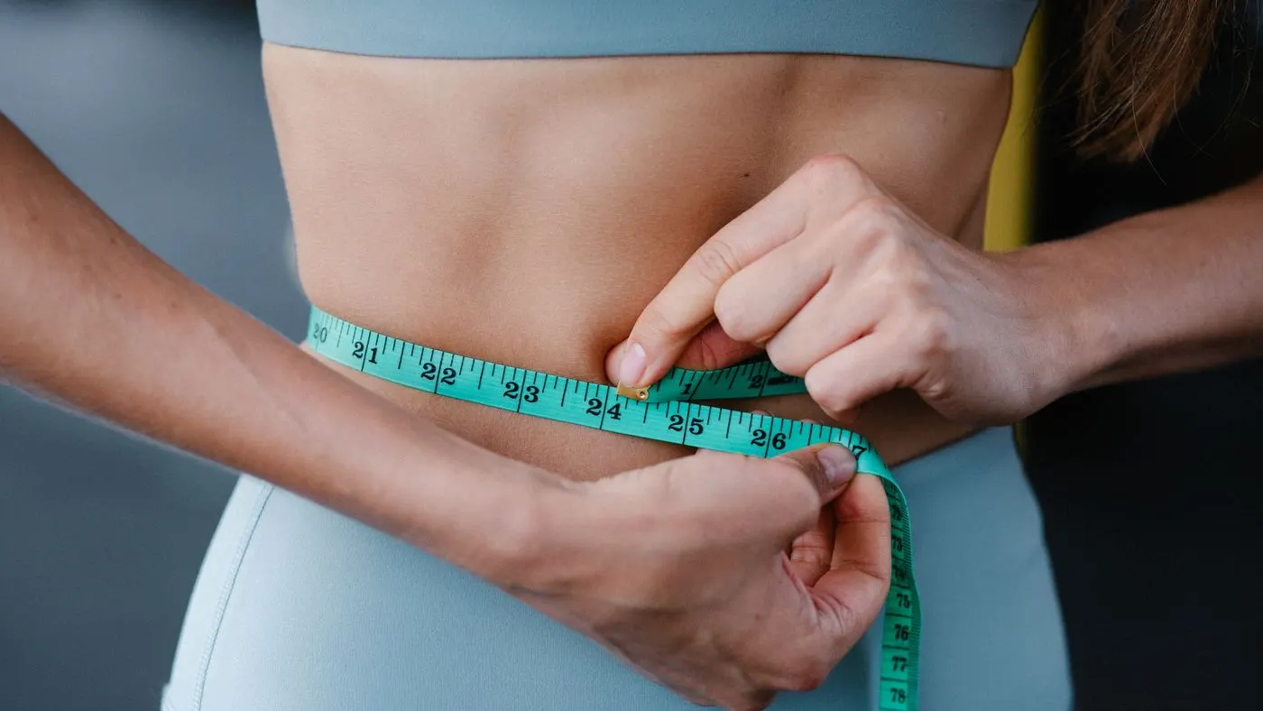 Primer plano de una mujer que mide el contorno de su cintura con una cinta métrica, medida que acompaña al IMC en los grados de obesidad
