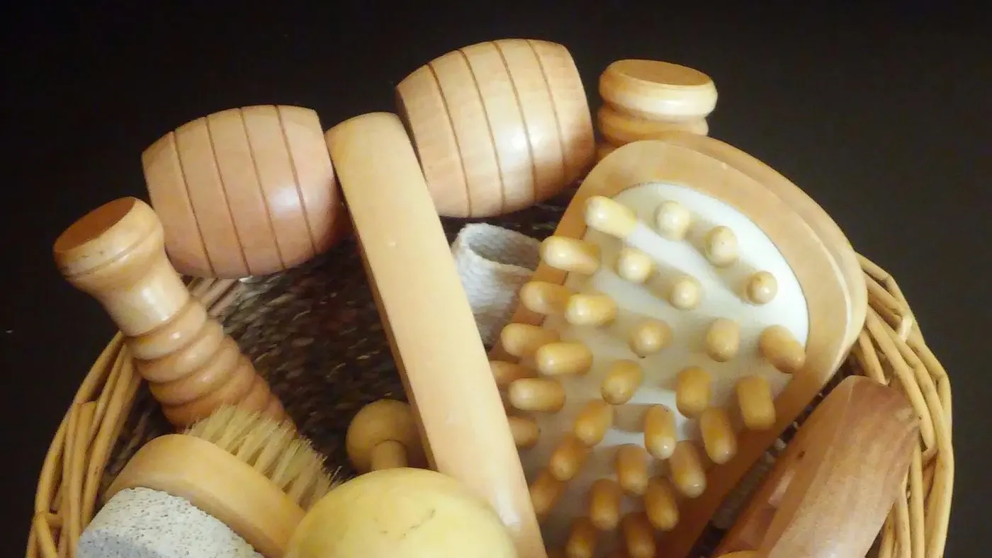 Instrumentos de madera para masaje, entre ellos rodillos, un masajeador de cuentas y una esfera, dentro de una canasta de mimbre, como los que se usan en la maderoterapia